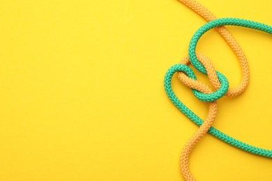 Photo of Colorful ropes tied in knot on yellow background, top view with space for text. Unity concept