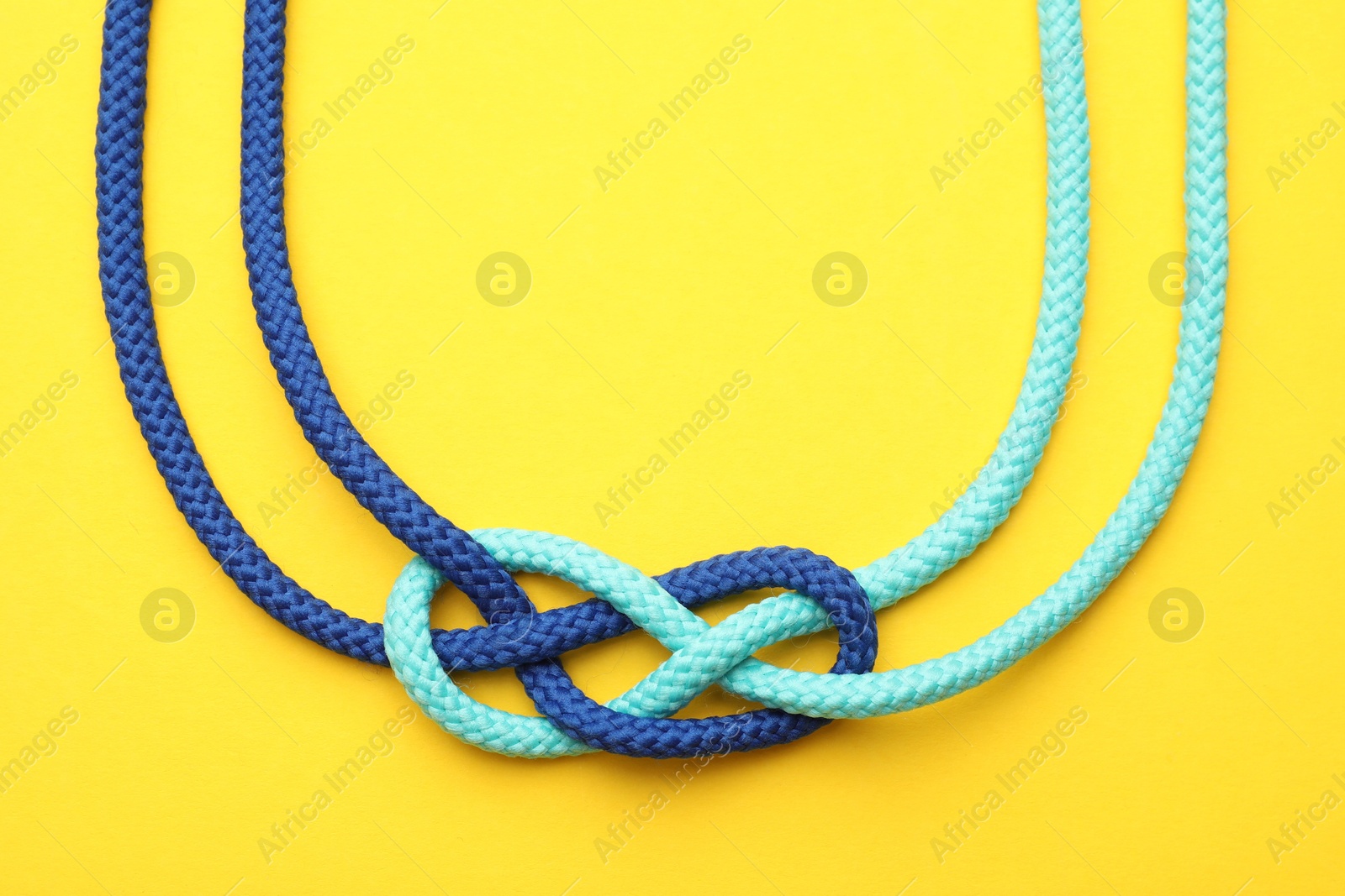 Photo of Colorful ropes tied in knot on yellow background, top view. Unity concept