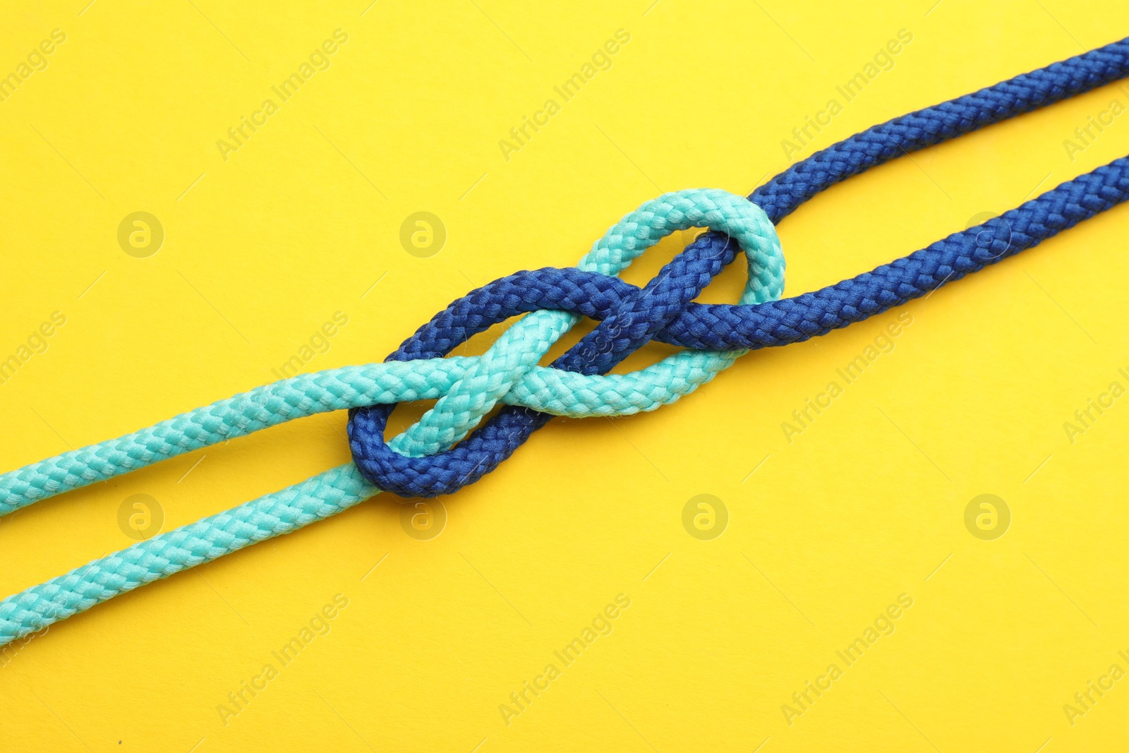 Photo of Colorful ropes tied in knot on yellow background, top view. Unity concept