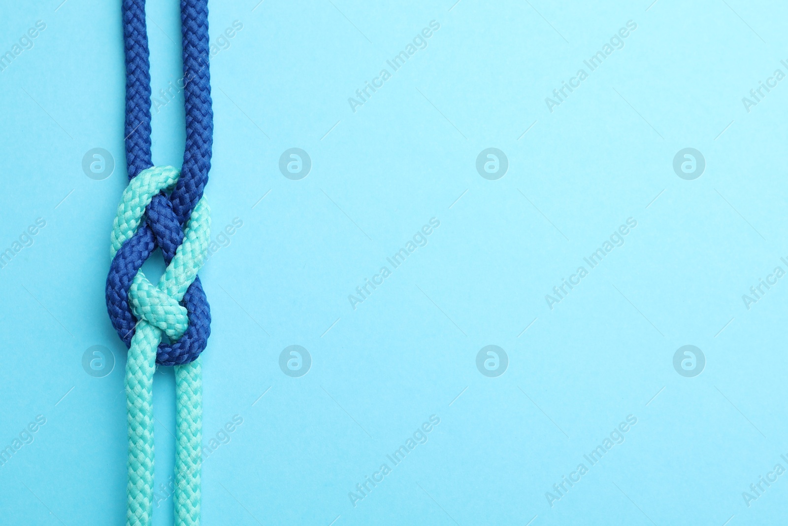 Photo of Colorful ropes tied in knot on light blue background, top view with space for text. Unity concept