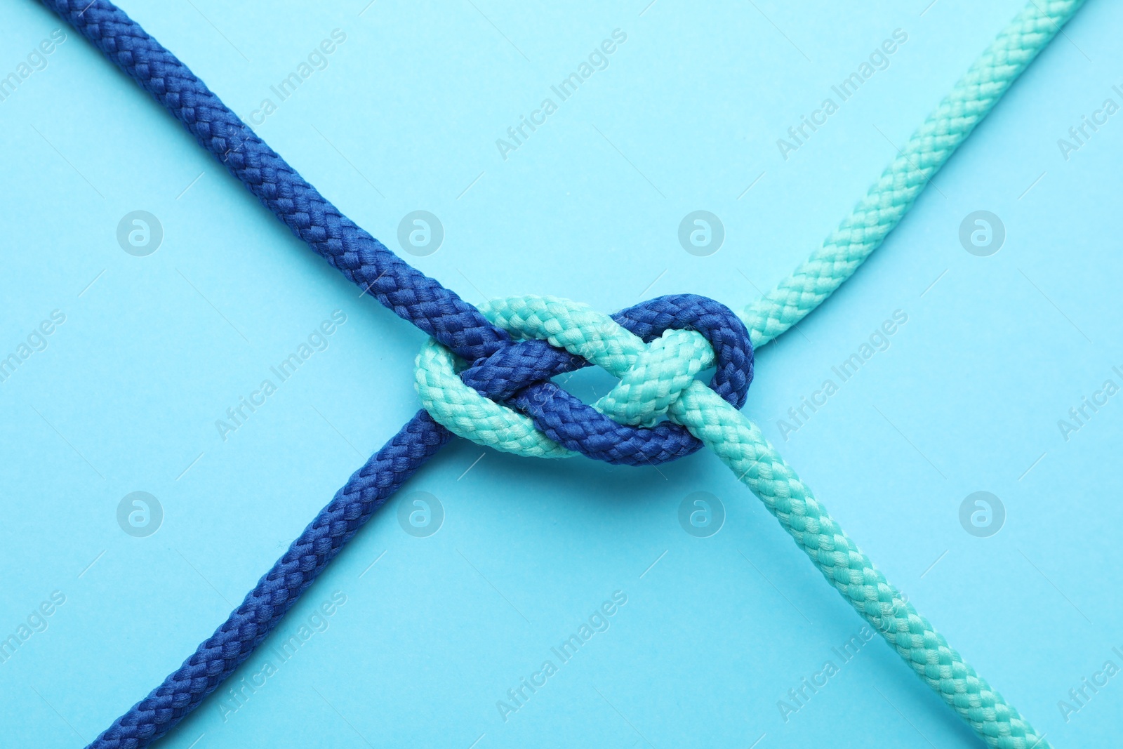 Photo of Colorful ropes tied in knot on light blue background, top view. Unity concept