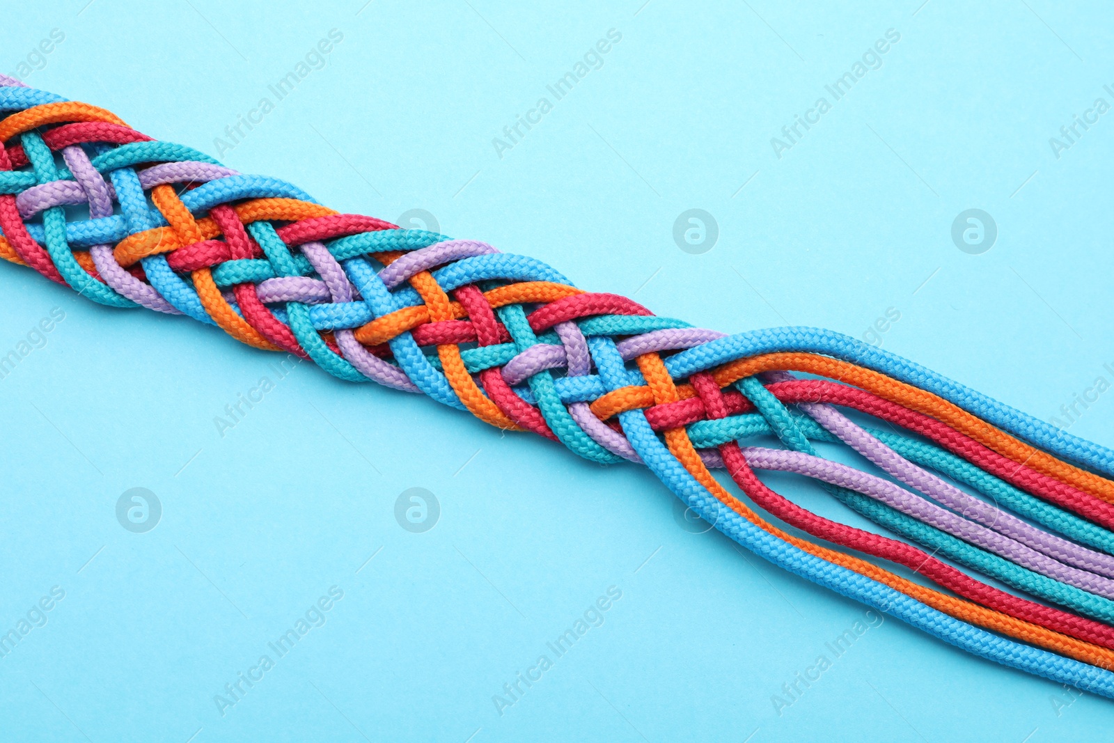 Photo of Braided colorful ropes on light blue background, top view. Unity concept