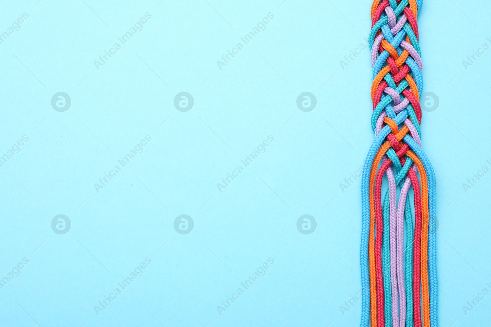 Photo of Braided colorful ropes on light blue background, top view with space for text. Unity concept