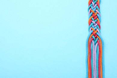 Photo of Braided colorful ropes on light blue background, top view with space for text. Unity concept