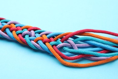 Photo of Braided colorful ropes on light blue background, closeup. Unity concept