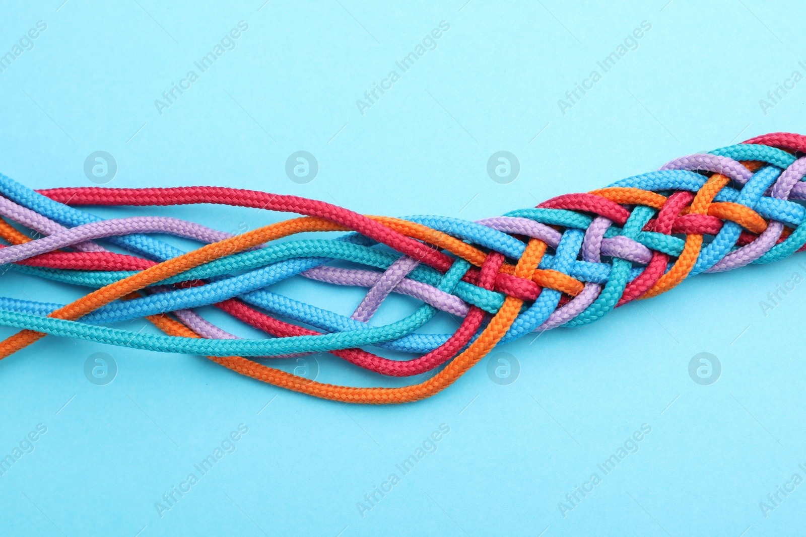 Photo of Braided colorful ropes on light blue background, top view. Unity concept