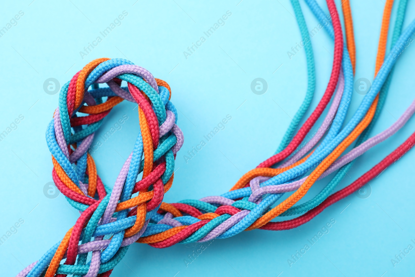 Photo of Braided colorful ropes on light blue background, top view. Unity concept