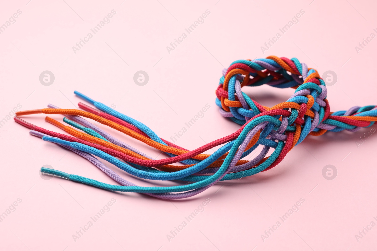 Photo of Braided colorful ropes on pink background, closeup. Unity concept