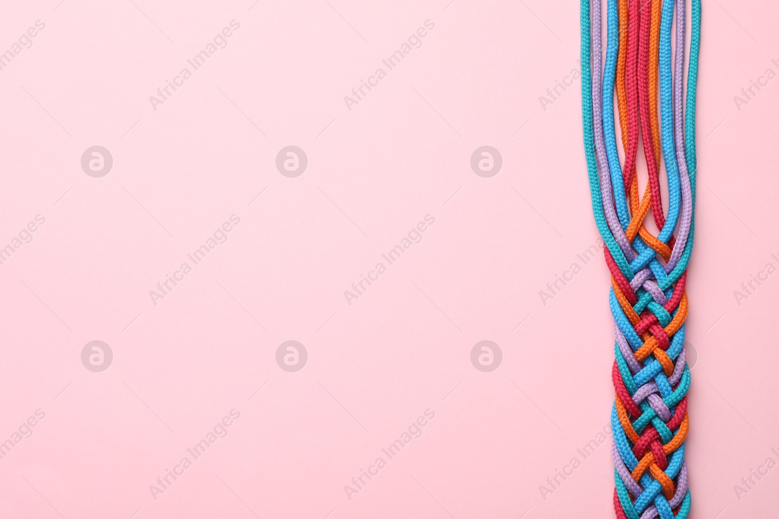 Photo of Braided colorful ropes on pink background, top view with space for text. Unity concept