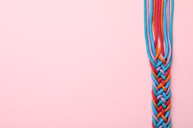 Photo of Braided colorful ropes on pink background, top view with space for text. Unity concept