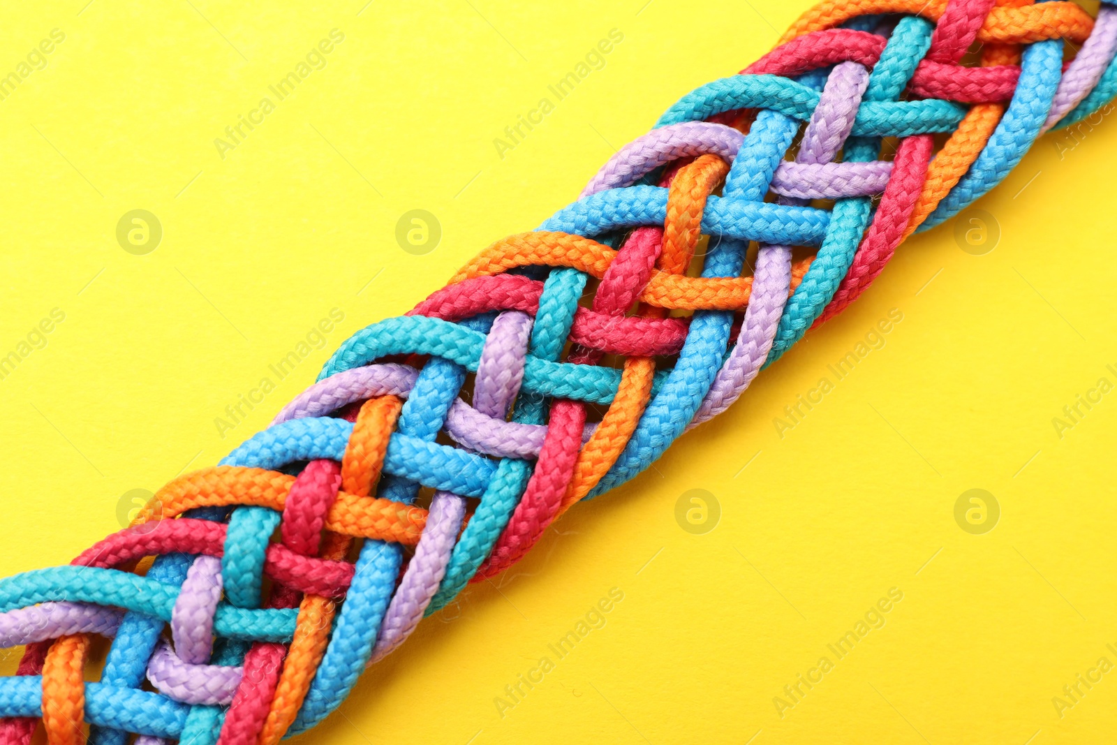 Photo of Braided colorful ropes on yellow background, top view. Unity concept