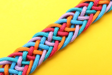 Photo of Braided colorful ropes on yellow background, top view. Unity concept