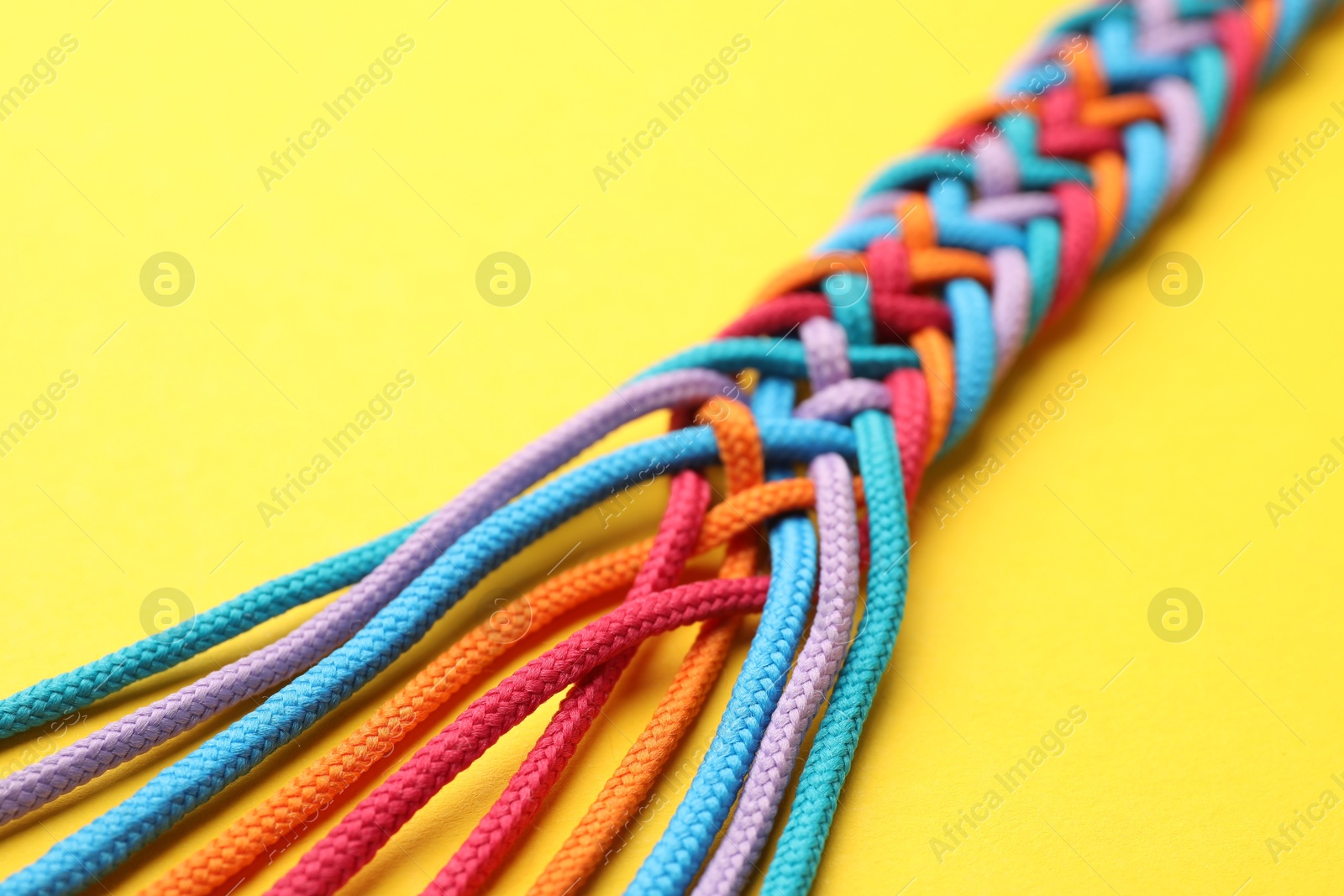 Photo of Braided colorful ropes on yellow background, closeup. Unity concept