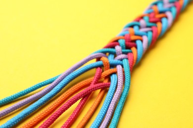 Photo of Braided colorful ropes on yellow background, closeup. Unity concept