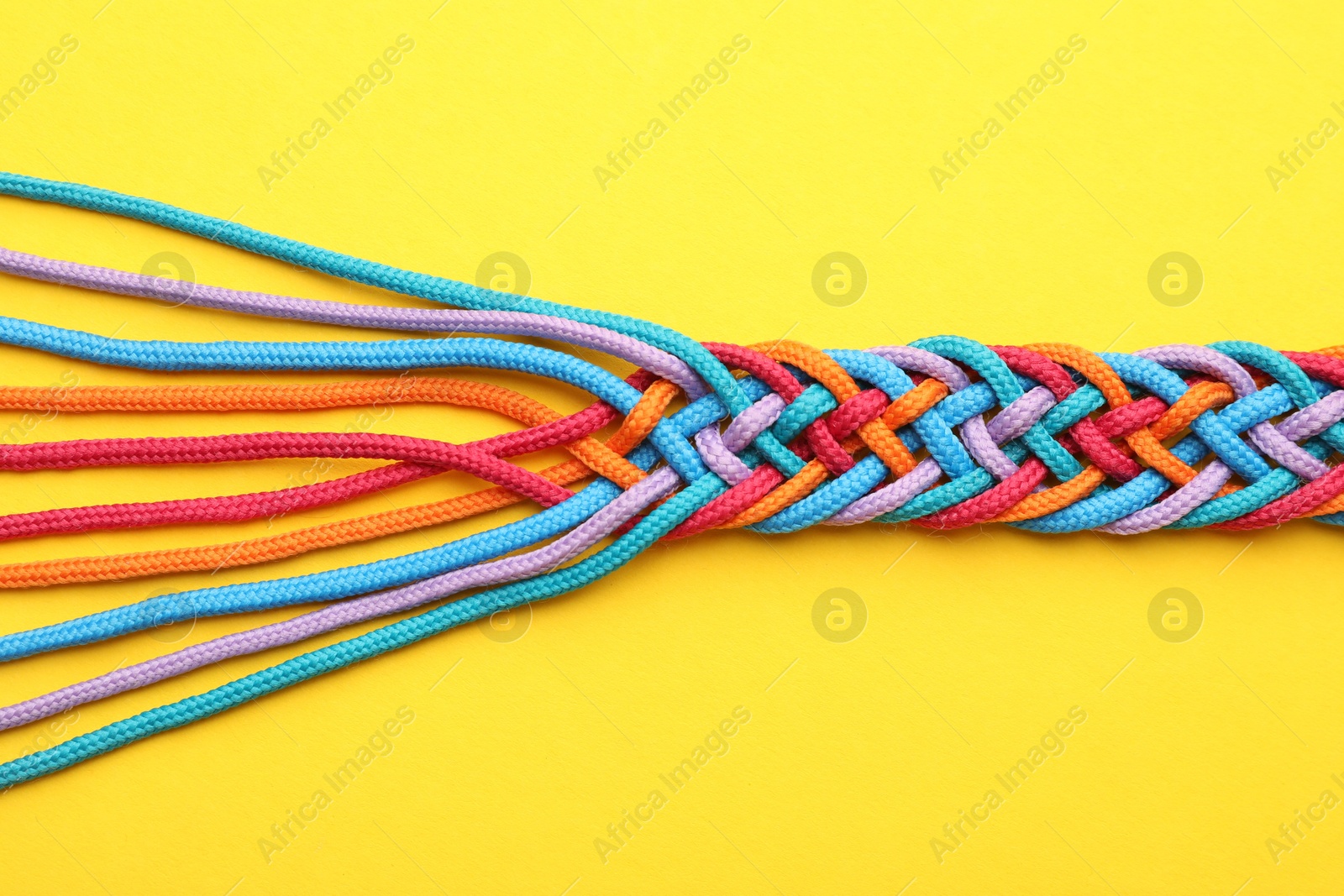 Photo of Braided colorful ropes on yellow background, top view. Unity concept