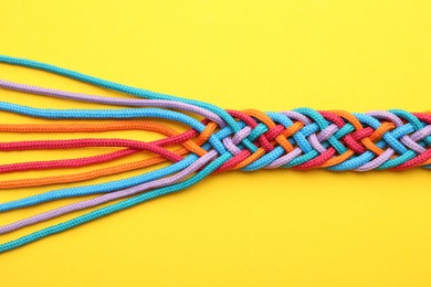 Photo of Braided colorful ropes on yellow background, top view. Unity concept