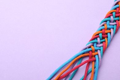 Photo of Braided colorful ropes on violet background, space for text. Unity concept