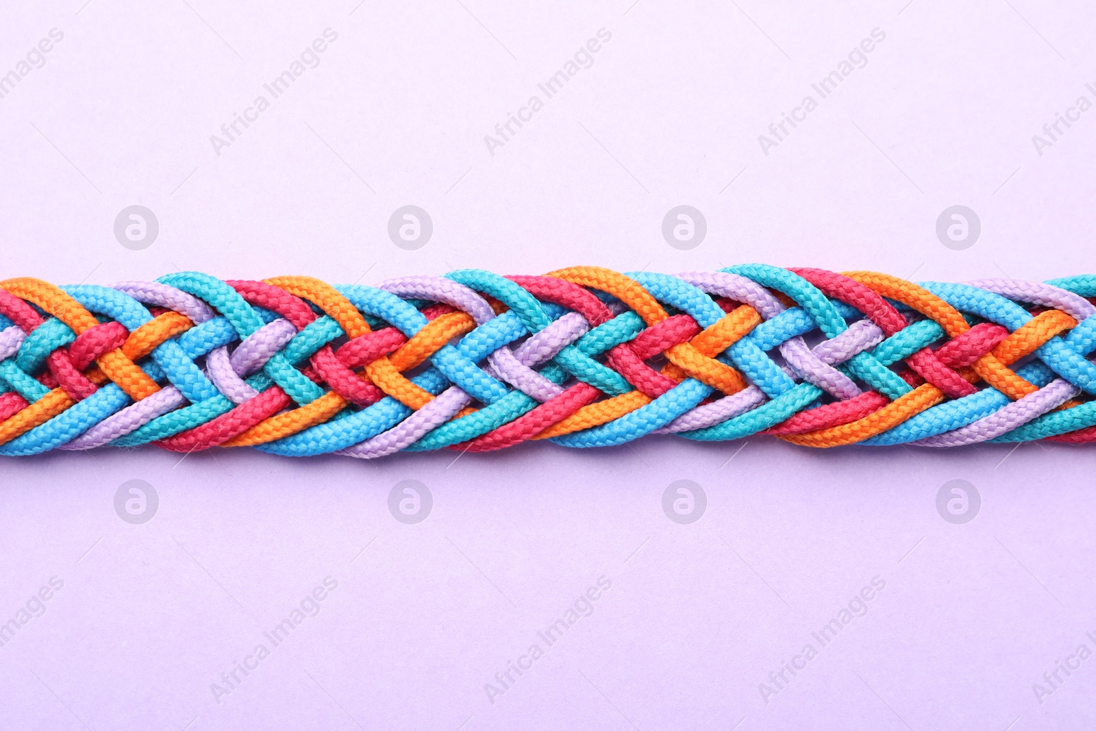 Photo of Braided colorful ropes on violet background, top view. Unity concept