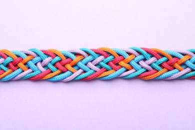 Photo of Braided colorful ropes on violet background, top view. Unity concept