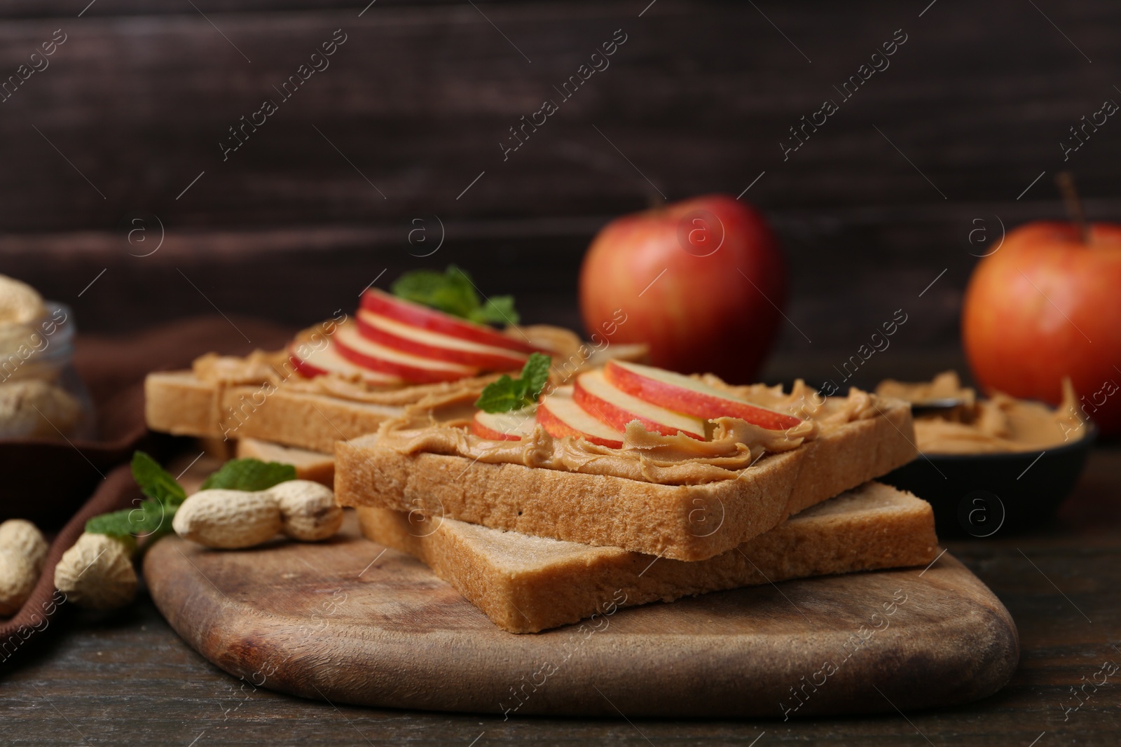 Photo of Tasty sandwiches with peanut butter, apples, nuts and mint on wooden table, closeup