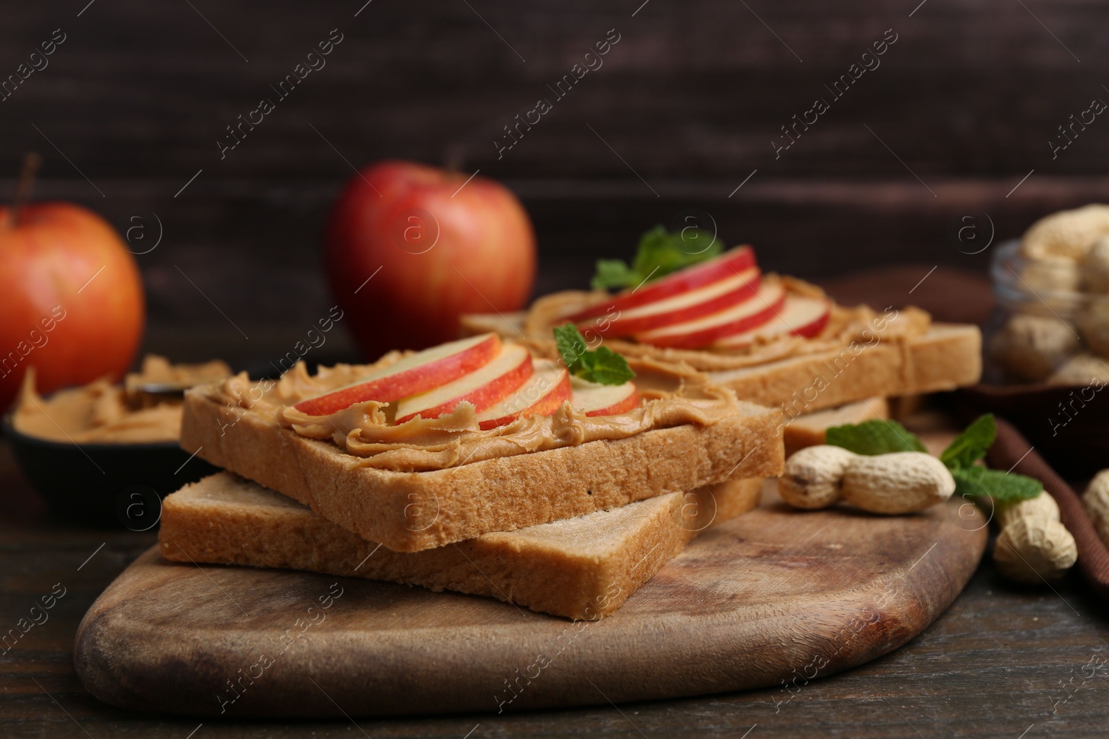 Photo of Tasty sandwiches with peanut butter, apples, nuts and mint on wooden table, closeup