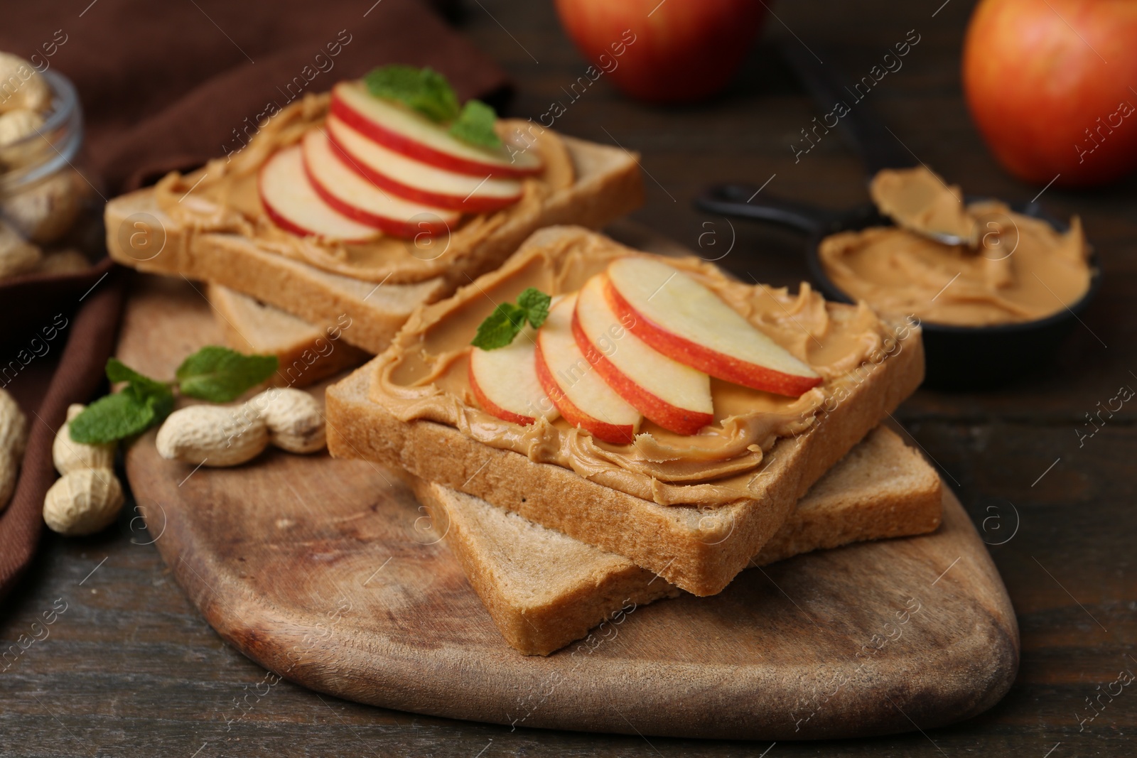 Photo of Tasty sandwiches with peanut butter, apples, nuts and mint on wooden table, closeup