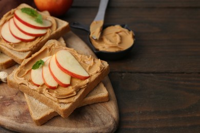 Photo of Tasty sandwiches with peanut butter, apple and mint on wooden table, closeup. Space for text