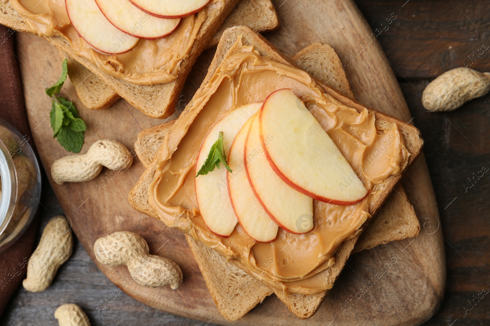 Photo of Tasty sandwiches with peanut butter, apple, nuts and mint on wooden table, flat lay