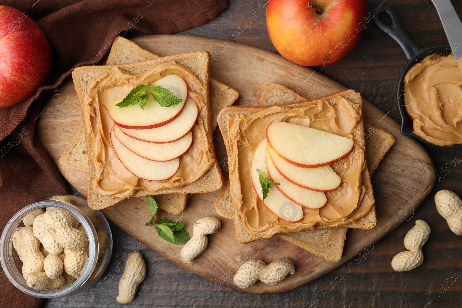 Photo of Tasty sandwiches with peanut butter, apples, nuts and mint on wooden table, flat lay