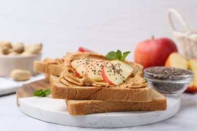 Photo of Tasty sandwiches with peanut butter, apple, chia seeds and mint on white table, closeup