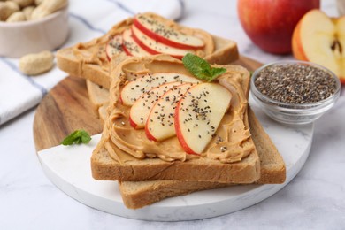 Photo of Tasty sandwiches with peanut butter, apple, chia seeds and mint on white marble table, closeup