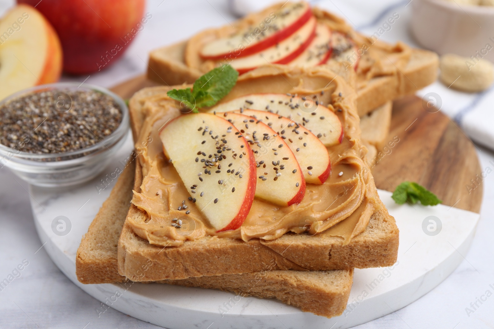 Photo of Tasty sandwiches with peanut butter, apple, chia seeds and mint on white table, closeup