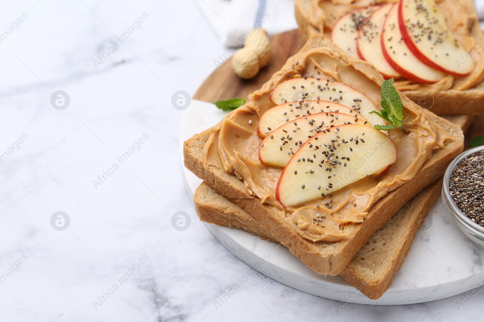 Photo of Tasty sandwiches with peanut butter, apple, chia seeds and mint on white marble table, closeup. Space for text