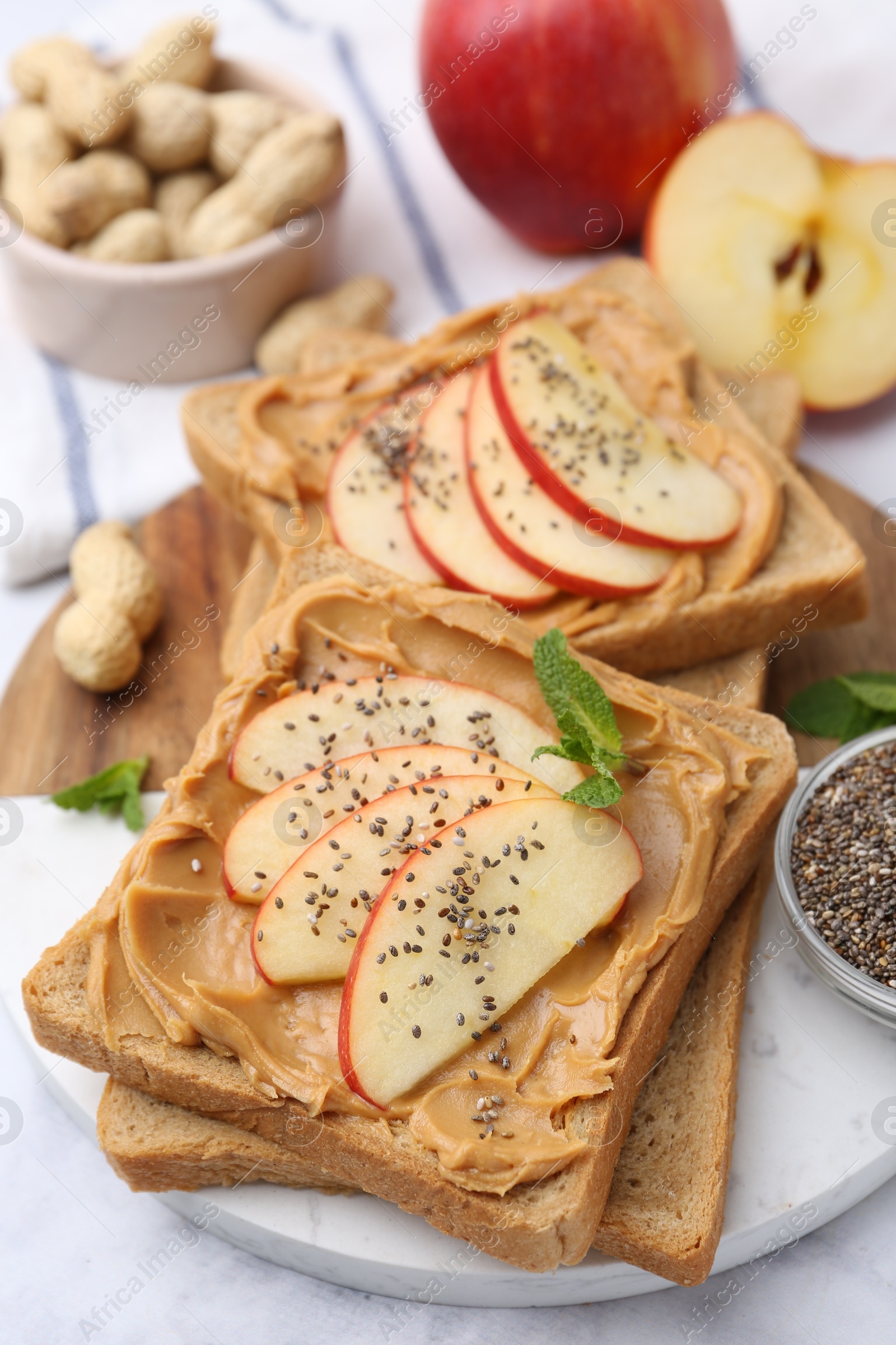 Photo of Tasty sandwiches with peanut butter, apple, chia seeds, nuts and mint on table, closeup