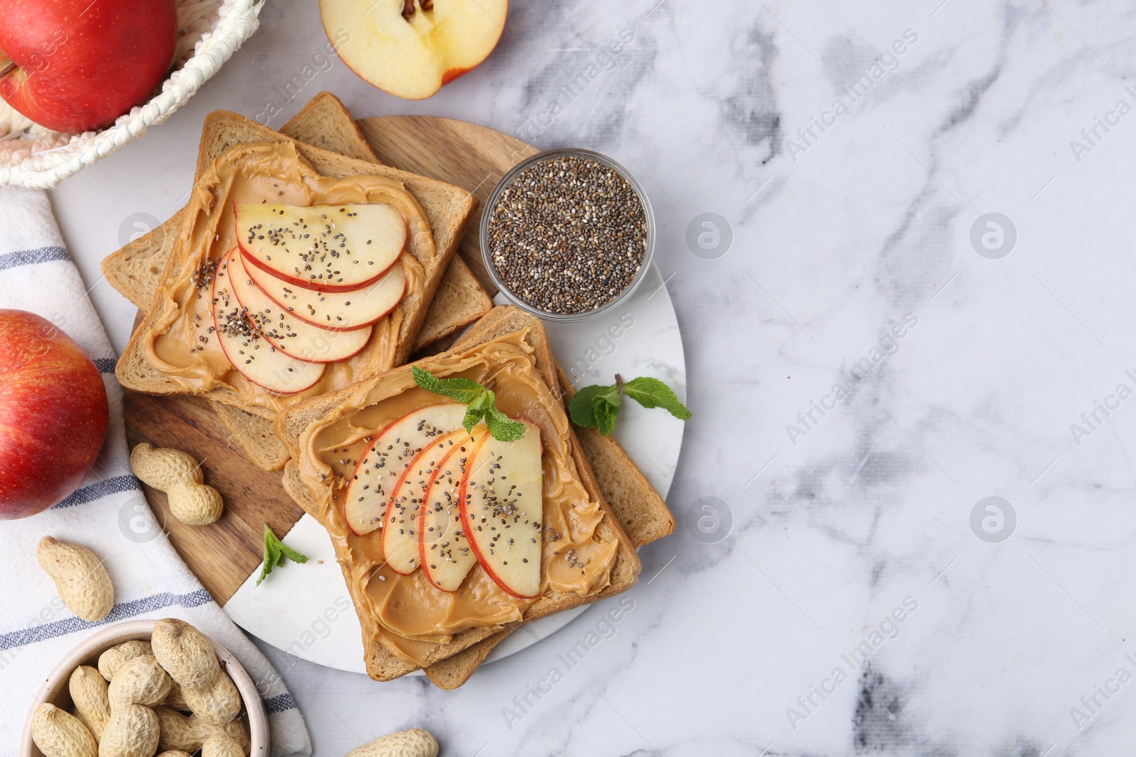 Photo of Tasty sandwiches with peanut butter, apples, chia seeds, nuts and mint on white marble table, flat lay. Space for text