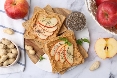 Photo of Tasty sandwiches with peanut butter, apples, chia seeds, nuts and mint on white marble table, flat lay