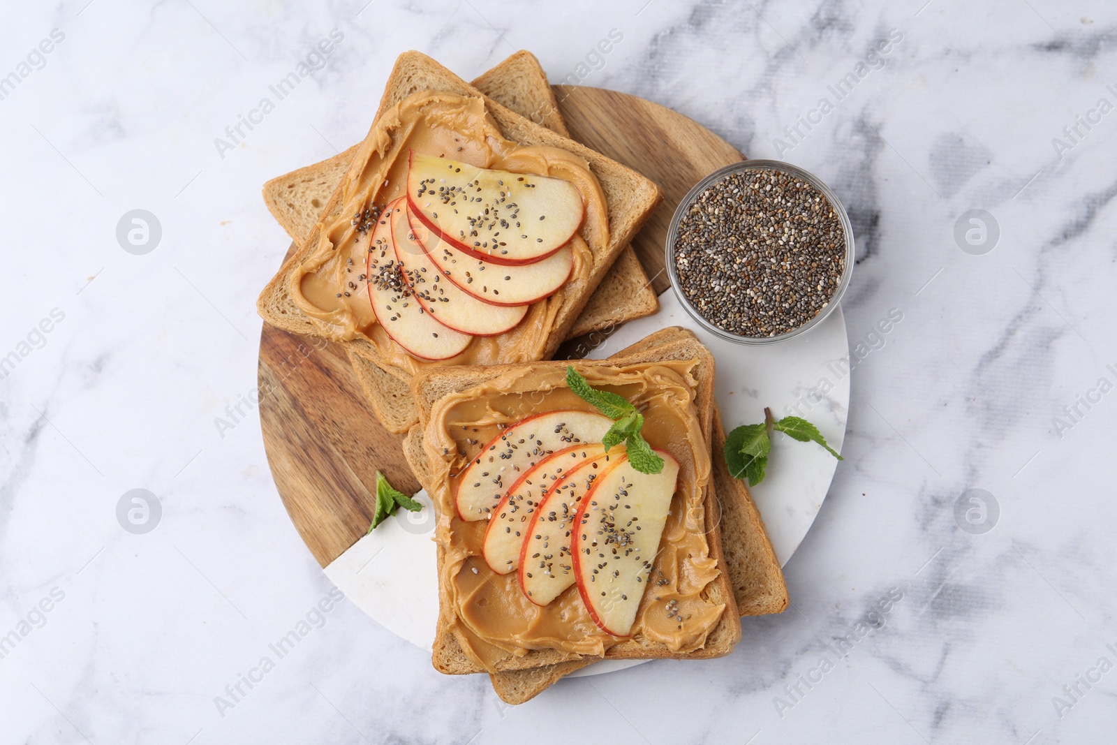 Photo of Tasty sandwiches with peanut butter, apple, chia seeds and mint on white marble table, top view