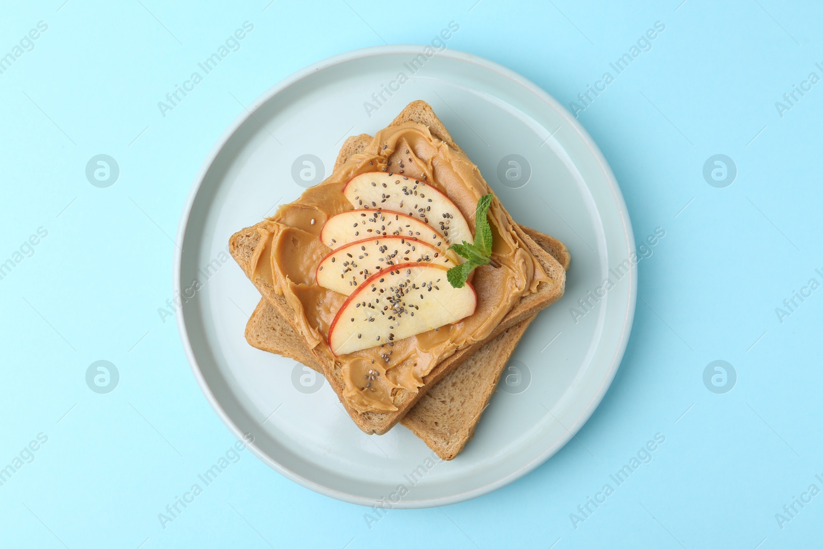 Photo of Tasty sandwich with peanut butter, apple, chia seeds and mint on light blue background, top view