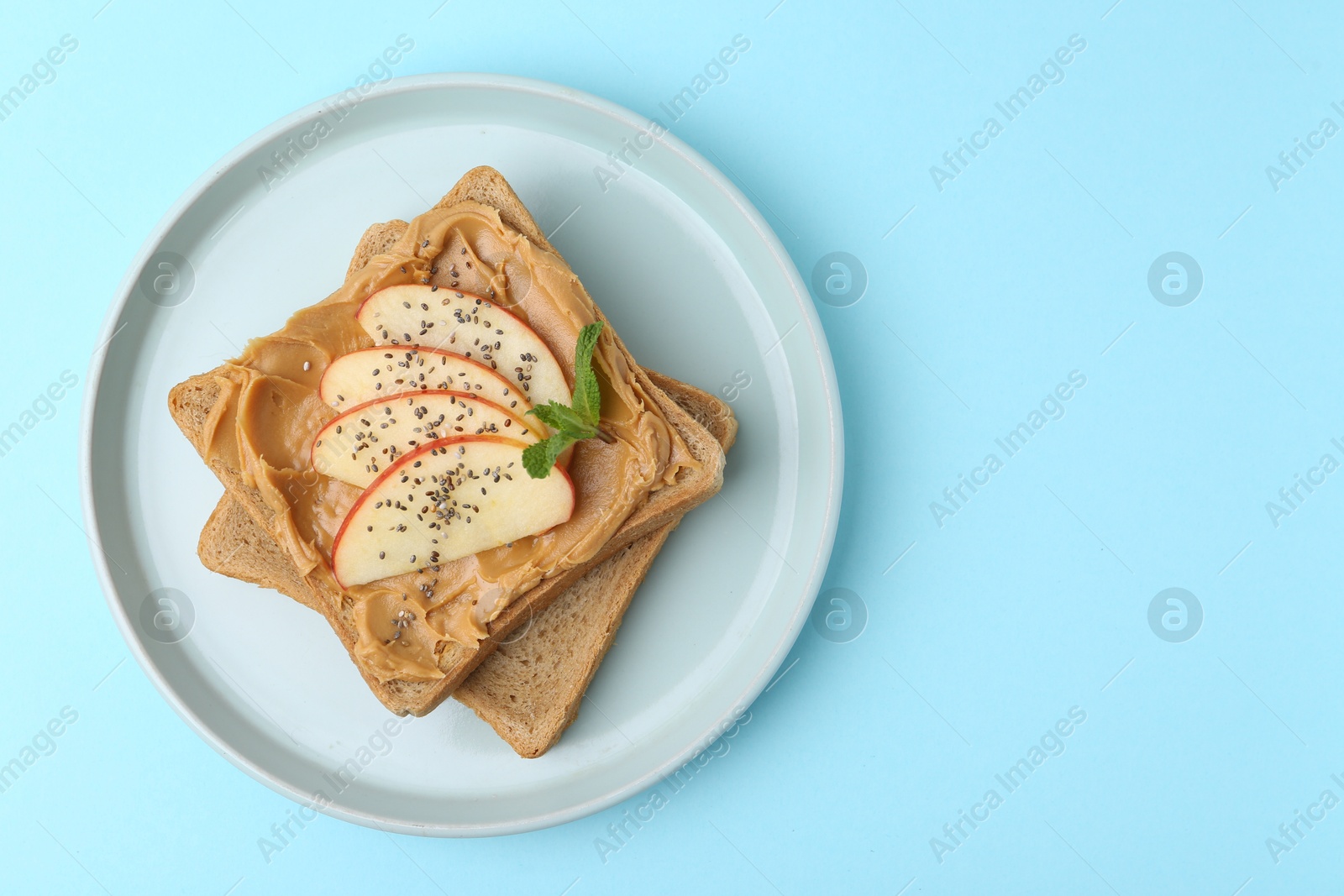 Photo of Tasty sandwich with peanut butter, apple, chia seeds and mint on light blue background, top view. Space for text