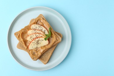 Photo of Tasty sandwich with peanut butter, apple, chia seeds and mint on light blue background, top view. Space for text