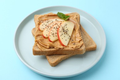 Photo of Tasty sandwich with peanut butter, apple, chia seeds and mint on light blue background, closeup