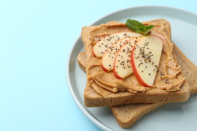 Photo of Tasty sandwich with peanut butter, apple, chia seeds and mint on light blue background, closeup. Space for text