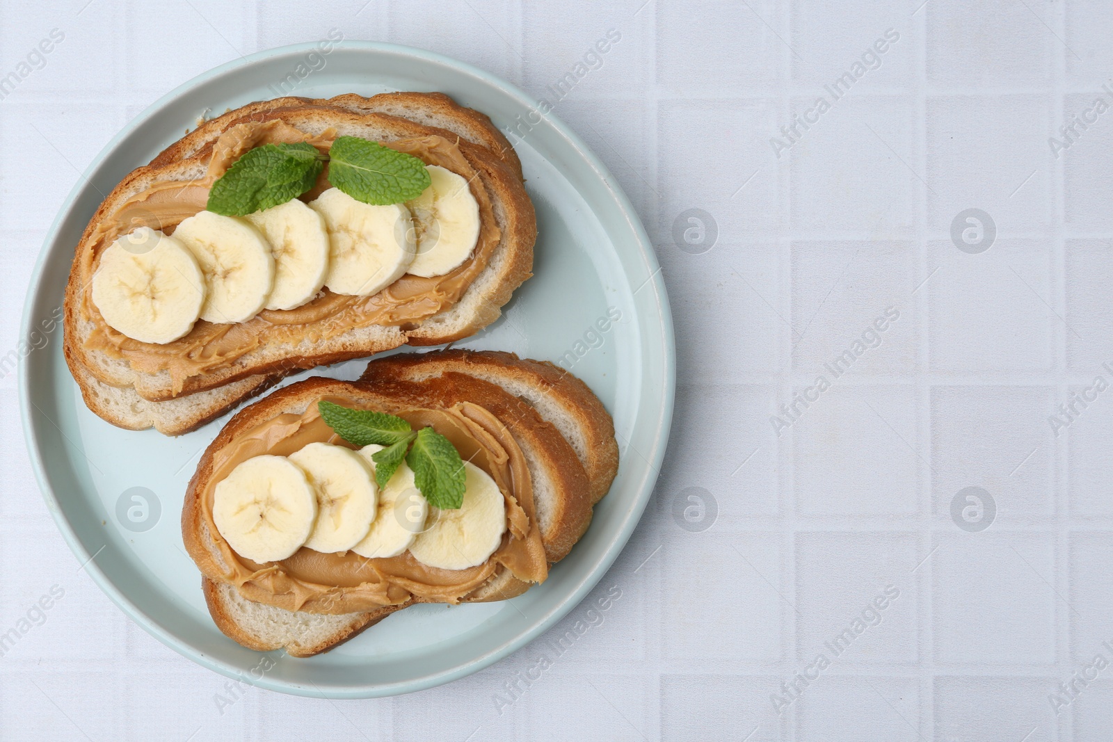 Photo of Tasty sandwiches with peanut butter, banana and mint on white tiled table, top view. Space for text