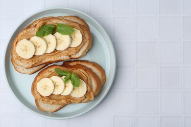 Photo of Tasty sandwiches with peanut butter, banana and mint on white tiled table, top view. Space for text