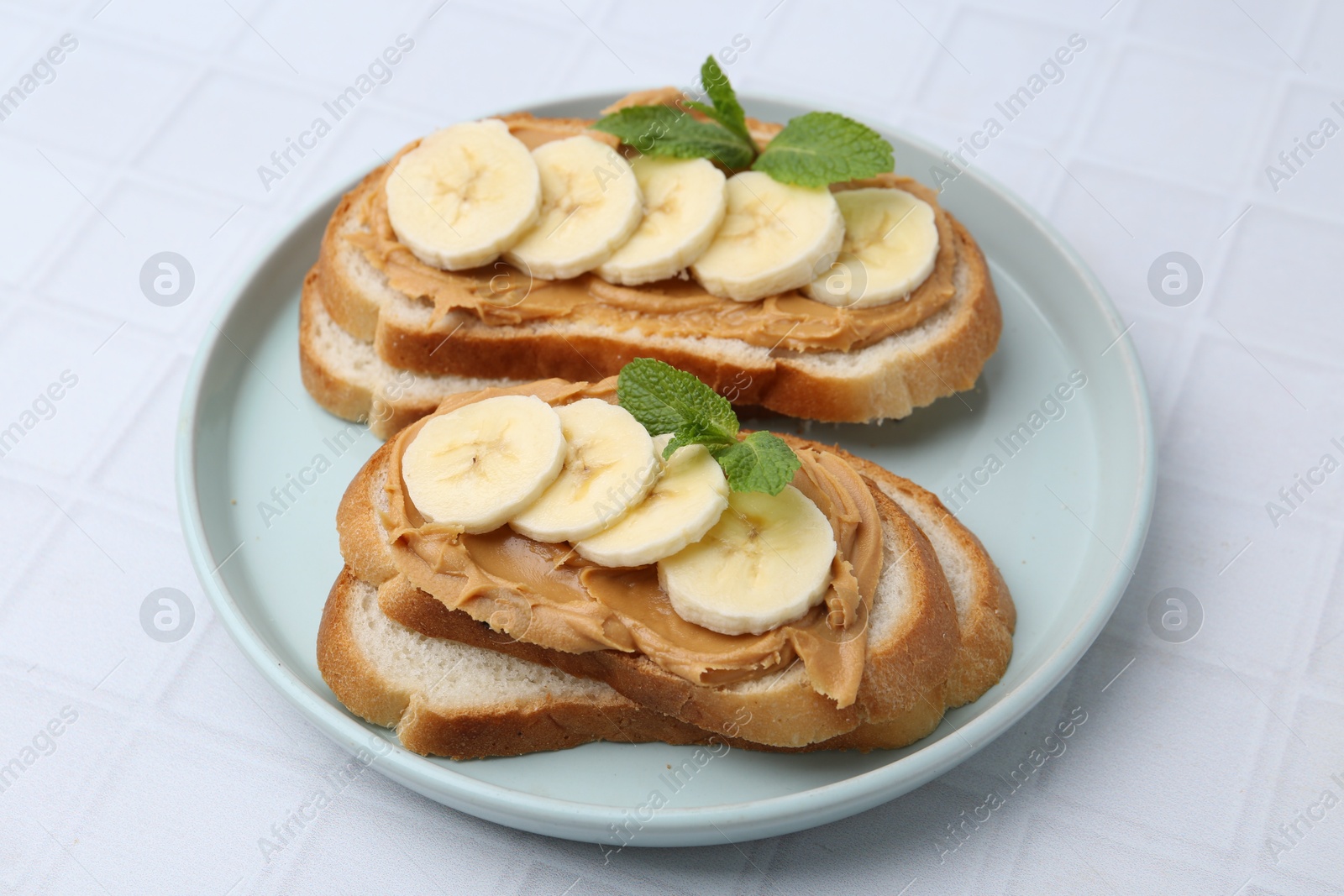 Photo of Tasty sandwiches with peanut butter, banana and mint on white tiled table, closeup