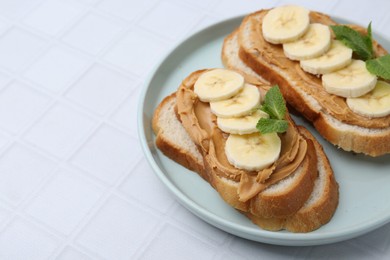 Photo of Tasty sandwiches with peanut butter, banana and mint on white tiled table, closeup. Space for text