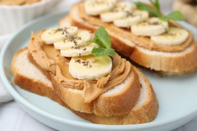 Photo of Tasty sandwiches with peanut butter, banana, chia seeds and mint on table, closeup