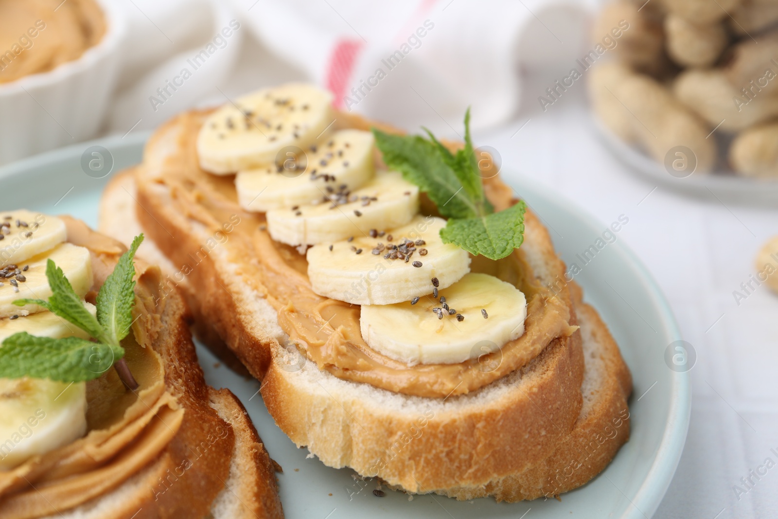 Photo of Tasty sandwiches with peanut butter, banana, chia seeds and mint on table, closeup