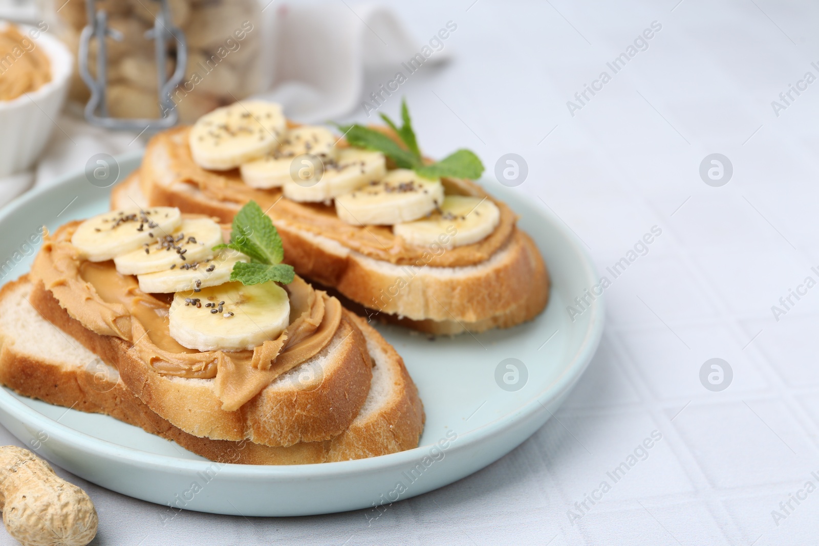 Photo of Tasty sandwiches with peanut butter, banana, chia seeds and mint on white tiled table, closeup