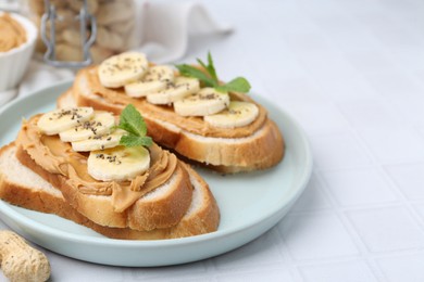 Photo of Tasty sandwiches with peanut butter, banana, chia seeds and mint on white tiled table, closeup